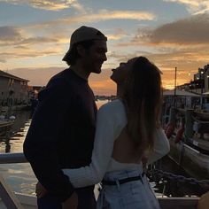 a man and woman standing next to each other in front of a body of water