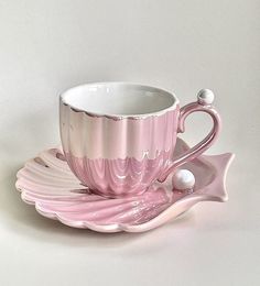 a pink coffee cup and saucer on a white tablecloth with pearls in the middle