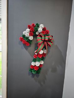 a christmas wreath hanging on the side of a gray wall with red and green pom - poms