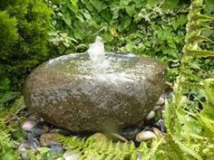 a water fountain in the middle of some plants and rocks with green foliage around it