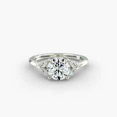 a white gold engagement ring with three stones on the side and a round brilliant diamond center