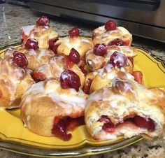 a yellow plate topped with pastries covered in icing and cherries on top of a counter