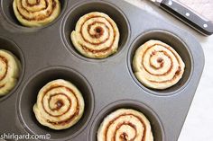 several cinnamon rolls in a muffin tin next to a knife