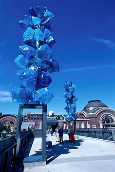 blue glass sculptures are on display in front of a building and some people walking down the sidewalk