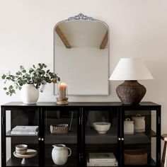 a table with a mirror, vases and other items on it next to a lamp