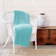 a white wicker chair with a blue knitted blanket on it next to a wooden chest