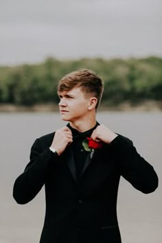 a young man in a tuxedo adjusts his bow tie on the beach