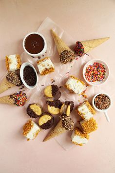 ice cream cones and desserts are arranged on a pink surface with confetti, sprinkles, and chocolate