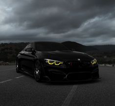 a black car parked in a parking lot under a cloudy sky with lights on it