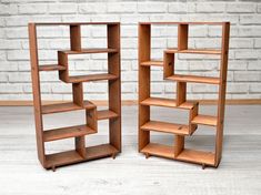 two bookshelves sitting next to each other on top of a wooden floor in front of a brick wall