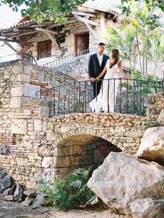 a bride and groom standing on a stone bridge