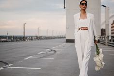 a woman is walking down the street with flowers in her hand and wearing a white suit