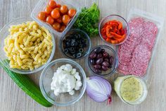 several different types of food in plastic containers on a wooden table with tomatoes, onions, cucumbers, olives, and other vegetables