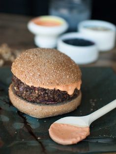 a close up of a hamburger on a plate with a spoon and dipping sauces