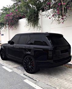 a black range rover parked in front of a white wall with pink flowers on it