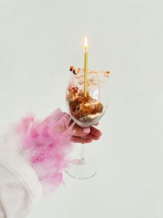 a person holding a wine glass with food in it and a candle sticking out of the top