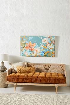 a couch sitting in front of a painting on the wall next to a vase and lamp