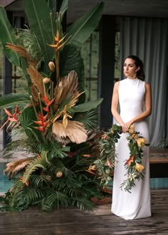 a woman in a white dress standing next to a tropical plant with red and yellow flowers