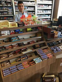 a man standing behind a counter in a store filled with snacks and candy bar items