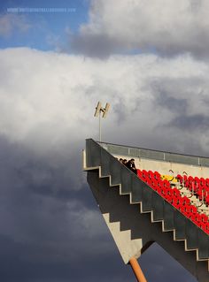 people are standing on the top of a bridge with red seats and railings in front of dark clouds