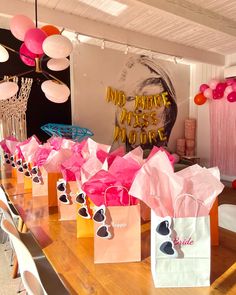 pink and white bags are lined up on a table with balloons in the background at a birthday party