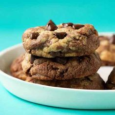 three chocolate chip cookies stacked on top of each other in a white bowl next to a blue background