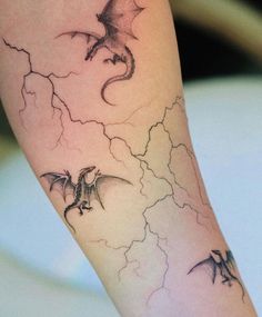 a tattoo on the leg of a woman with two bats flying through the sky and lightning behind her