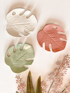 three leaf shaped paper plates sitting on top of a table next to flowers and leaves