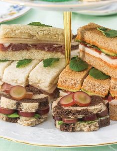 several sandwiches are stacked on a white plate with gold trimmings and green leafy garnishes