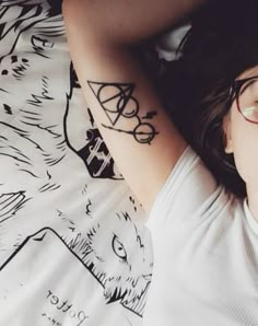 a woman with glasses laying on top of a bed next to a bear and arrow tattoo