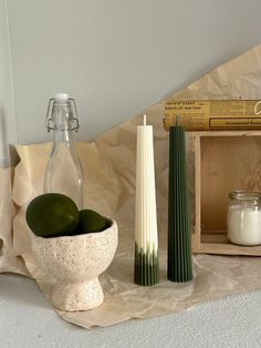 two green apples in a white bowl next to some candles and other items on a table