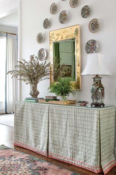 a table with plates and vases on it in front of a wall mounted mirror