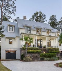 a large white house with lots of windows and plants on the front lawn, surrounded by trees