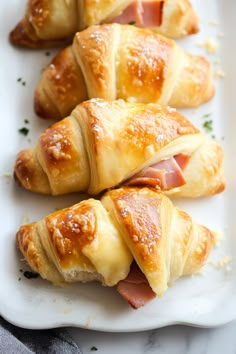 several croissants with ham and cheese on them sitting on a white plate