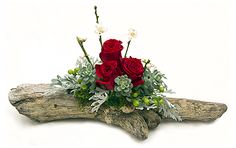 a bouquet of red roses sitting on top of a piece of driftwood with succulents and greenery