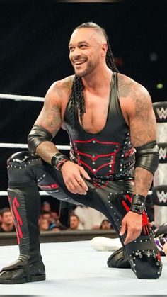 a man with long hair and tattoos sitting on top of a wrestling ring wearing black leather pants