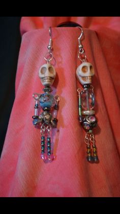 two pairs of earrings with skulls and beads hanging from them on a pink fabric background