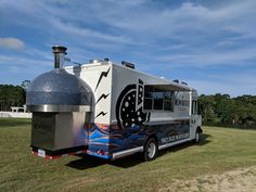 a food truck parked on the side of a road in front of trees and grass