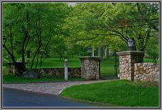 a stone fence and gate in front of a lush green park