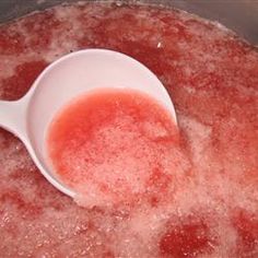 a white spoon in a pot filled with water and red liquid on the inside of it