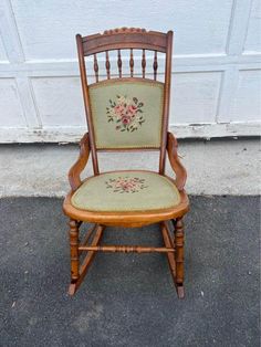 an old wooden rocking chair with needled flowers on the back and seat, sitting in front of a garage door