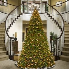 a large christmas tree in the middle of a room with stairs and banisters