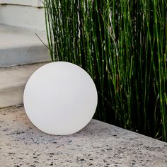 a white ball sitting on top of a cement slab next to some tall green grass