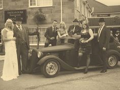 a group of people that are standing in front of an old fashioned car and posing for the camera