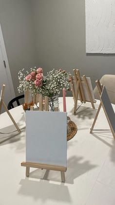 a white table topped with a vase filled with pink roses and flowers next to easels