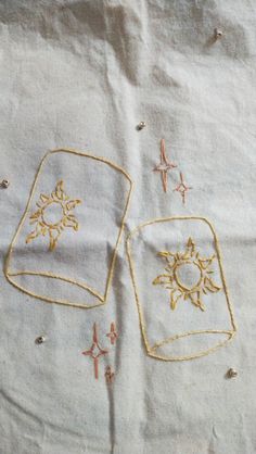 two embroidered square designs on a white sheet with gold thread and starbursts