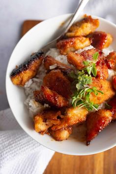 a white bowl filled with chicken and rice on top of a wooden table next to a fork