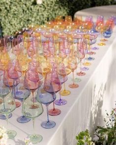 many wine glasses are lined up on a long table with flowers in the back ground