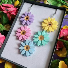 three flower earrings in a box with flowers around them on the table next to each other