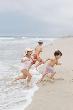 two children running on the beach with one child wearing a hat